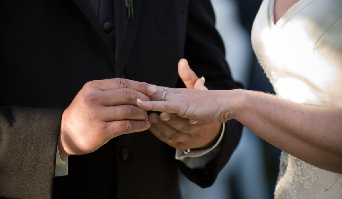 Up close image of bride putting a ring on a bride's finger