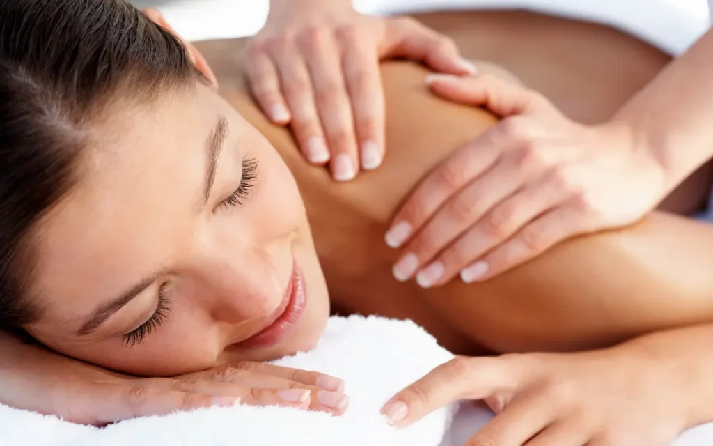 Stock image of a girl getting a massage showing her closed eyes, smilig with hands on her shoulder